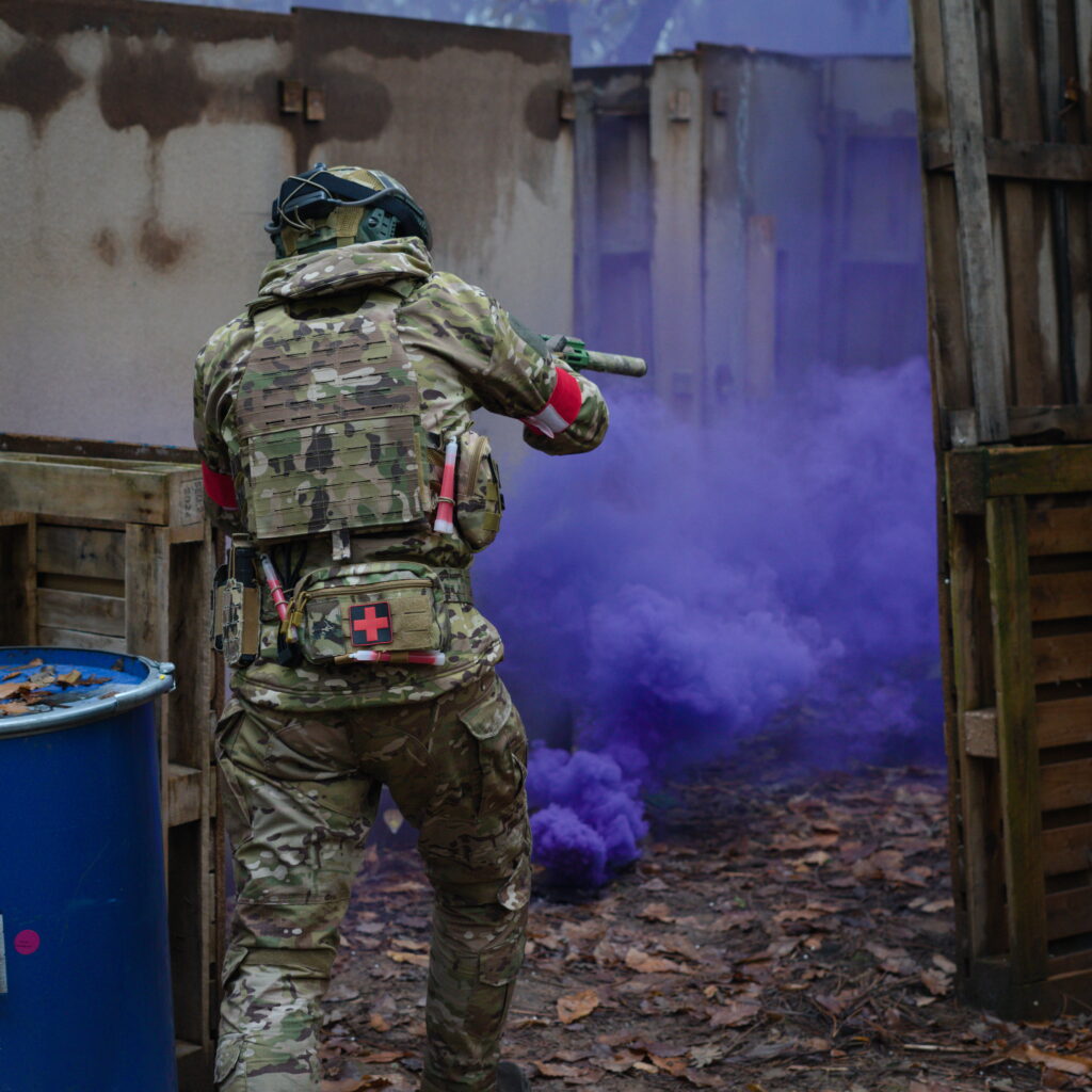 Joueur d’airsoft progressant dans un bâtiment sous la couverture d’un fumigène violet lors d’un scénario tactique en Dordogne.