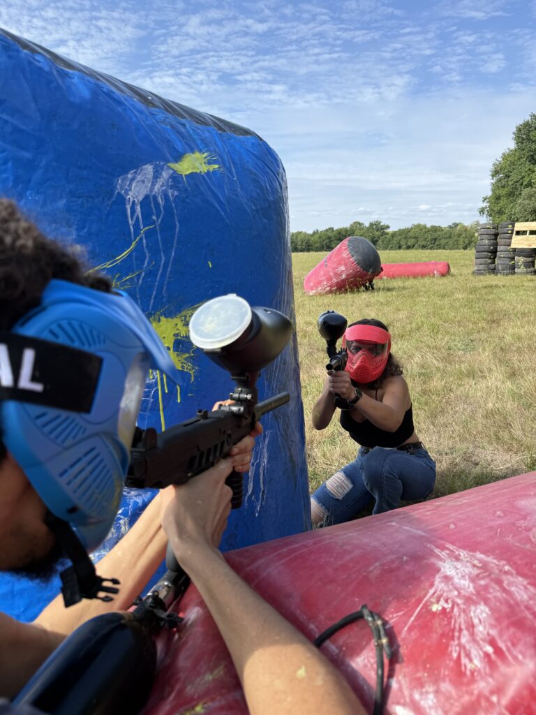Joueurs en duel de paintball derrière des obstacles gonflables sur un terrain extérieur en Dordogne.