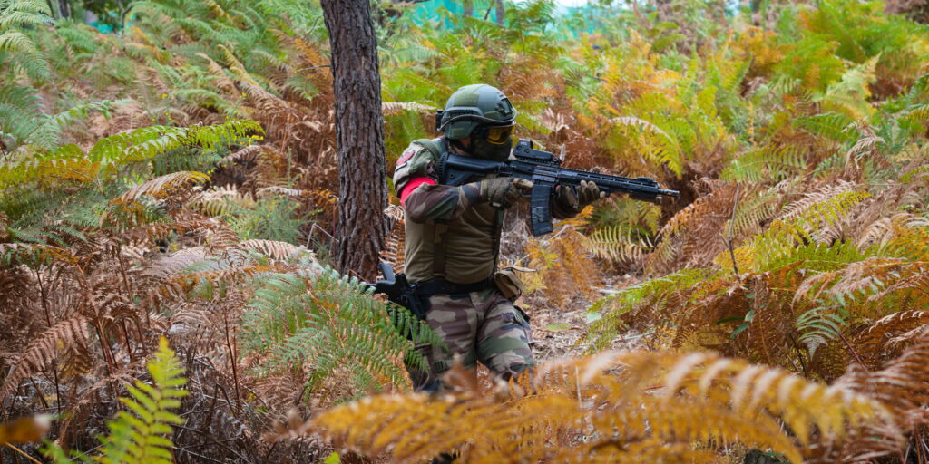 Joueur d’airsoft progressant dans une forêt de fougères lors d’un scénario tactique immersif en Dordogne.