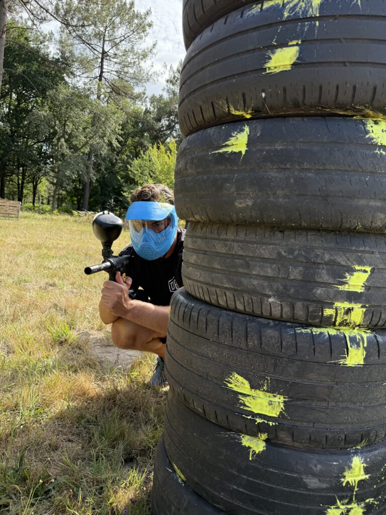 Joueur de paintball utilisant un obstacle en pneus comme couverture sur un terrain extérieur en Dordogne.