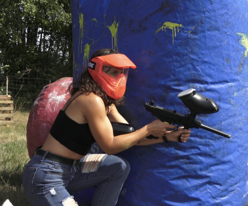 Joueuse de paintball en action derrière un obstacle gonflable sur un terrain extérieur en Dordogne.
