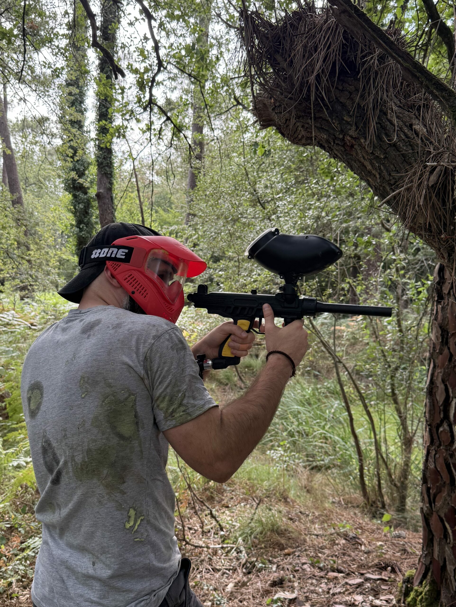 Joueur de paintball utilisant un arbre comme couverture lors d’une partie en forêt en Dordogne.