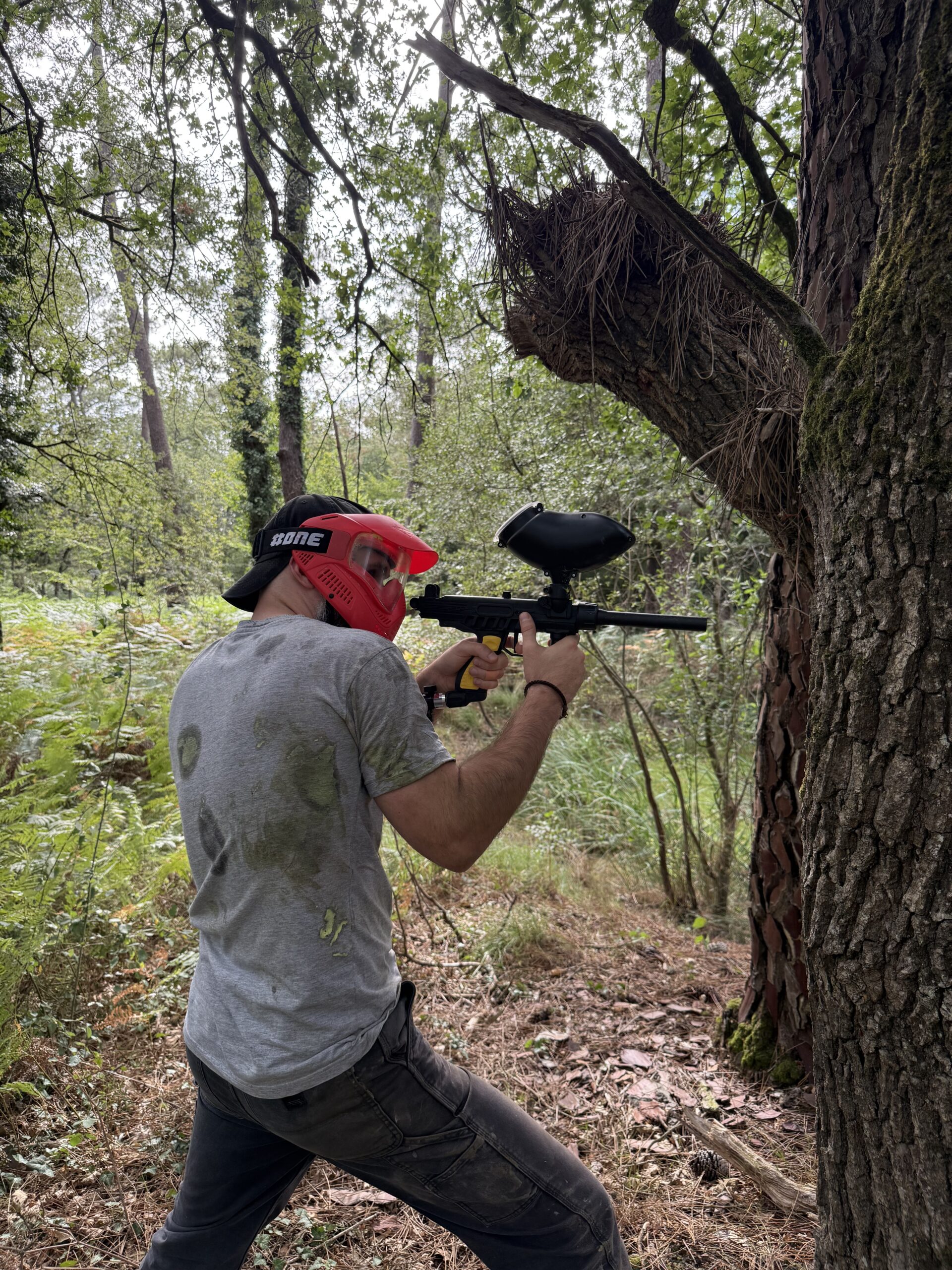 Joueur de paintball utilisant un arbre comme couverture lors d’une partie en forêt en Dordogne.