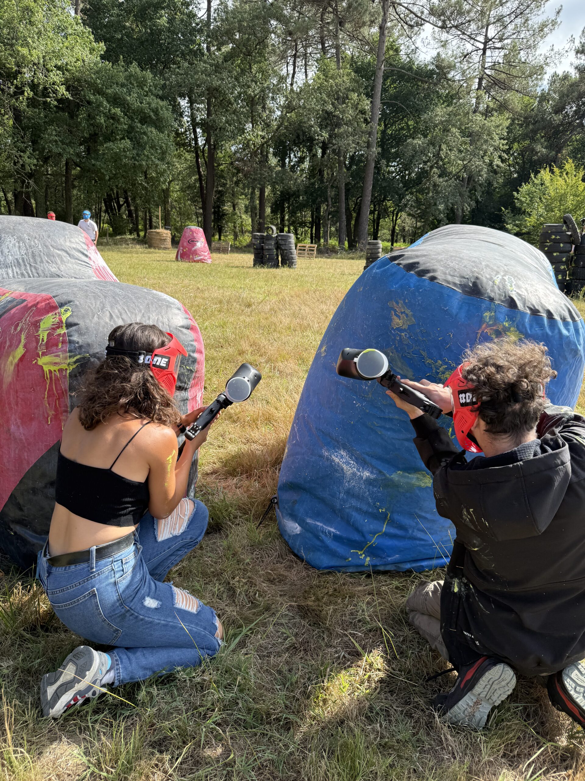 Deux joueurs de paintball en équipe derrière des obstacles gonflables lors d’une partie sur un terrain en Dordogne.